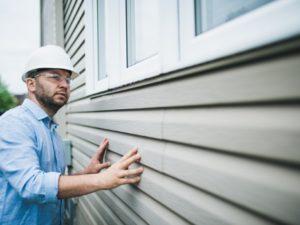 A home remodeling contractor inspects his work on the exterior of a grey home. 